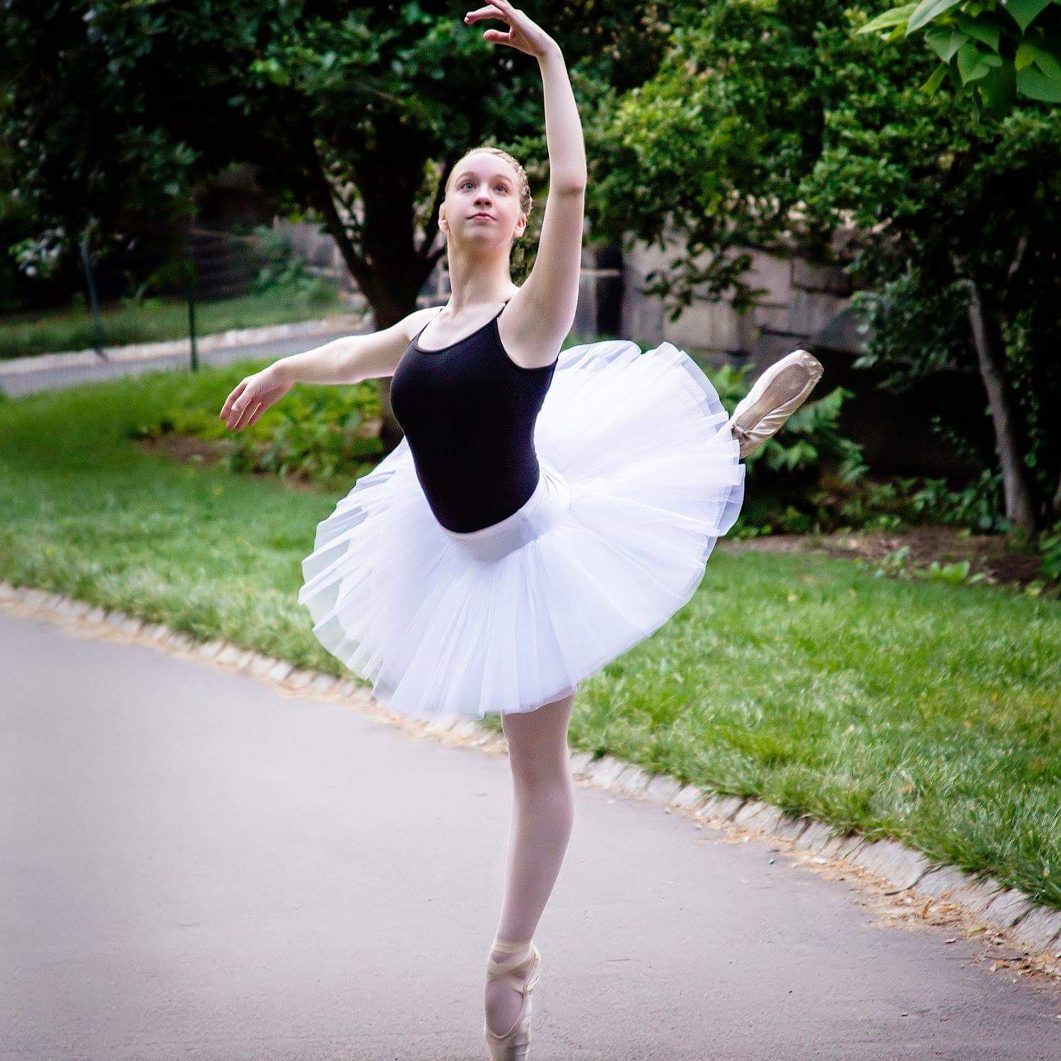 Jessica in an attitude ballet position on pointe in a park.